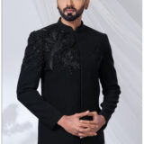 Man wearing a black embroidered Jodhpuri suit with detailed bird motifs on the shoulder and chest.