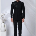 Man wearing a black embroidered Jodhpuri suit with detailed bird motifs on the shoulder and chest.