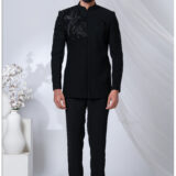 Man wearing a black embroidered Jodhpuri suit with detailed bird motifs on the shoulder and chest.