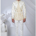 Man wearing an ivory white Jodhpuri suit with golden peacock and floral embroidery, styled with a mandarin collar.