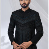 Man wearing a black Jodhpuri suit with intricate geometric embroidery in blue and black tones.