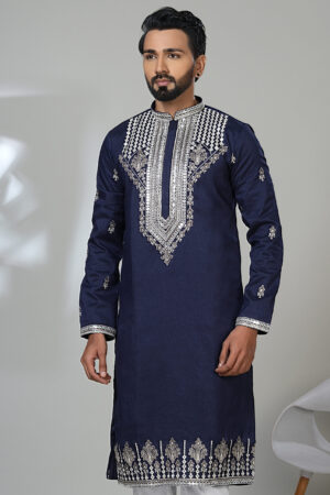 Man wearing a navy blue kurta with heavy silver embroidery on the chest, sleeves, and hem, styled with white pants and black shoes.