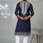 Man wearing a navy blue kurta with heavy silver embroidery on the chest, sleeves, and hem, styled with white pants and black shoes.