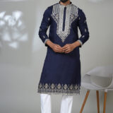 Man wearing a navy blue kurta with heavy silver embroidery on the chest, sleeves, and hem, styled with white pants and black shoes.