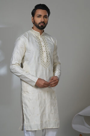 Man wearing an ivory embroidered kurta with intricate front placket and all-over floral accents, styled with white pants and black formal shoes.