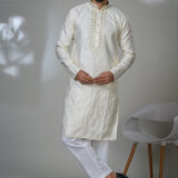 Man wearing an ivory embroidered kurta with intricate front placket and all-over floral accents, styled with white pants and black formal shoes.