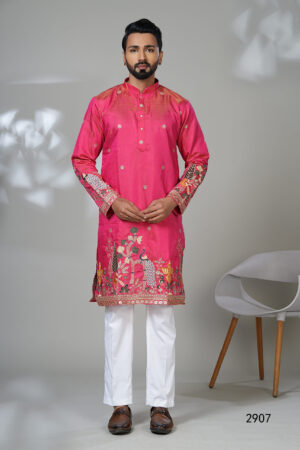 Man wearing a vibrant pink embroidered kurta with intricate floral and peacock designs, paired with white trousers and brown leather shoes, standing against a neutral background.