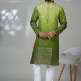 Man wearing a multicolor floral printed kurta with mirror work embroidery on the neckline, paired with white trousers and black loafers, standing indoors against a neutral backdrop.