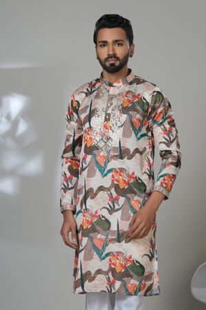 Man wearing a multicolor floral printed kurta with mirror work embroidery on the neckline, paired with white trousers and black loafers, standing indoors against a neutral backdrop.