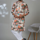 Man wearing a multicolor floral printed kurta with mirror work embroidery on the neckline, paired with white trousers and black loafers, standing indoors against a neutral backdrop.