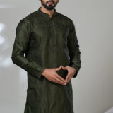 Man wearing a deep olive green embroidered kurta with tonal detailing and a band collar, paired with white trousers and black loafers, standing indoors against a neutral backdrop.