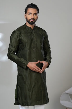 Man wearing a deep olive green embroidered kurta with tonal detailing and a band collar, paired with white trousers and black loafers, standing indoors against a neutral backdrop.