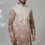 Man wearing a taupe kurta with white and copper peacock embroidery, white pants, and brown loafers — an artistic and regal ethnic outfit.