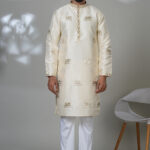 Man wearing an ivory silk kurta with gold elephant embroidery, white trousers, and brown shoes — perfect for festive or formal Indian wear.