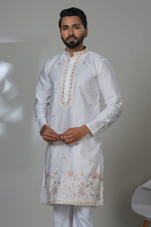 an in a white kurta with floral embroidery and mirror accents, worn with white trousers and black shoes.
