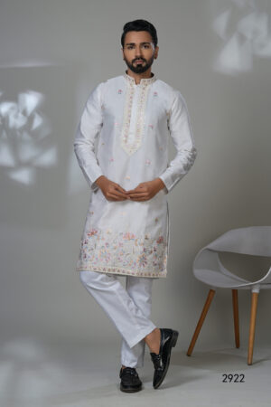 Man in a white kurta with floral embroidery and mirror accents, worn with white trousers and black shoes.