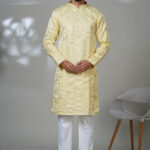 Man in a lemon-yellow kurta with geometric mirror embroidery, paired with white trousers and black shoes.