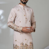 Man in a light pink kurta with intricate floral embroidery on the hem and sleeves, worn with white pants.