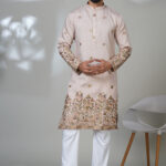 Man in a light pink kurta with intricate floral embroidery on the hem and sleeves, worn with white pants.