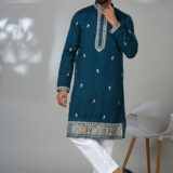 Man wearing a teal kurta with mirror embroidery and elephant motif border, paired with white pants.