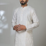 Man in an ivory kurta with mirror work and white pants, styled in a modern ethnic look.