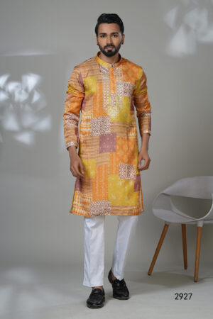 Man in a vibrant patchwork-printed kurta in shades of orange and yellow, styled with white pants and black loafers.