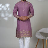 Man wearing a mauve kurta with gold ethnic embroidery and white trousers, posing in a minimalistic indoor setting.