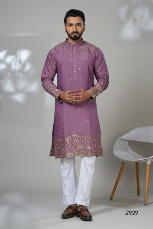 Man wearing a mauve kurta with gold ethnic embroidery and white trousers, posing in a minimalistic indoor setting.