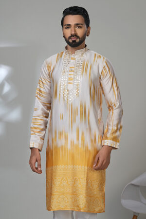 Man wearing a yellow and white ombre kurta with embroidery and white trousers, standing in a modern room with a white chair.