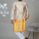 Man wearing a yellow and white ombre kurta with embroidery and white trousers, standing in a modern room with a white chair.