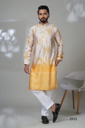 Man wearing a yellow and white ombre kurta with embroidery and white trousers, standing in a modern room with a white chair.