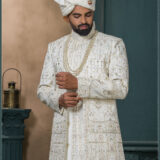 Groom in an ivory sherwani with architectural and floral embroidery, styled with layered pearl necklaces and an elegant traditional look.