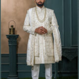 Groom in an ivory sherwani with architectural and floral embroidery, styled with layered pearl necklaces and an elegant traditional look.