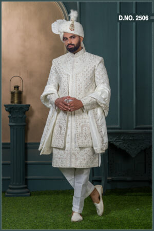 Groom in an ivory sherwani with geometric and floral zari embroidery, styled with a white turban adorned with feather and jewel embellishment.