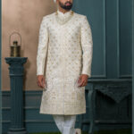 Ivory sherwani with gold embroidery and peacock design for groom wedding wear.