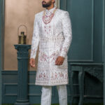 Ivory sherwani with heritage embroidery featuring royal motifs of elephants and musicians for wedding wear.