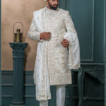 Ivory sherwani with pastel thread and zardozi embroidery, worn with traditional turban and feather adornment.