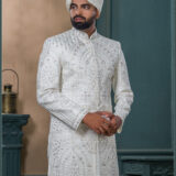 Ivory sherwani with architectural embroidery and subtle bead detailing, styled with a traditional turban and feather.