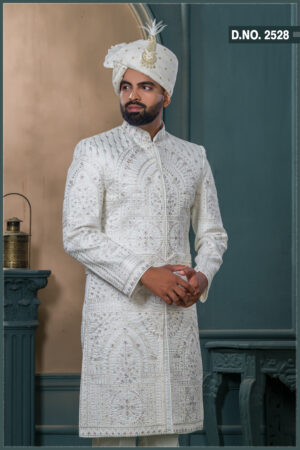 Ivory sherwani with architectural embroidery and subtle bead detailing, styled with a traditional turban and feather.