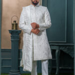 Ivory sherwani with architectural embroidery and subtle bead detailing, styled with a traditional turban and feather.