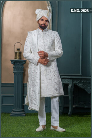 Ivory sherwani with architectural embroidery and subtle bead detailing, styled with a traditional turban and feather.