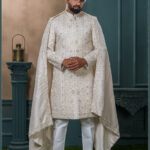 Ivory mirror-work sherwani with intricate embroidery, styled with a white turban and feather for a royal groom look.