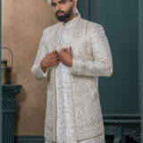 Ivory sherwani with intricate gold zardozi embroidery and turban with feather, styled for an elegant groom look.