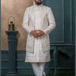 Ivory sherwani with intricate gold zardozi embroidery and turban with feather, styled for an elegant groom look.