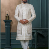 Ivory sherwani with intricate gold zardozi embroidery and turban with feather, styled for an elegant groom look.