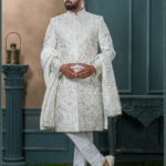 Ivory sherwani with silver and blue embroidered peacock motifs, paired with a cream turban featuring feather embellishment.