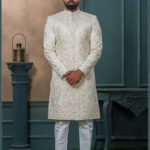 Ivory sherwani with detailed thread and zari embroidery, paired with a matching ivory turban featuring gold embellishment and feather accent.