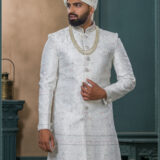Ivory textured sherwani with silver and pink embroidery, paired with an ivory turban embellished with pearls and a feather accent.