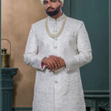 Ivory sherwani with intricate zari pattern, paired with an ivory turban featuring pearl and feather embellishment, and a layered pearl necklace.