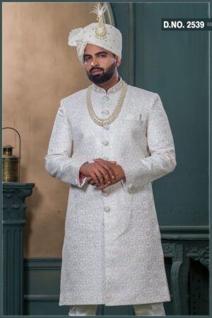 Ivory sherwani with intricate zari pattern, paired with an ivory turban featuring pearl and feather embellishment, and a layered pearl necklace.